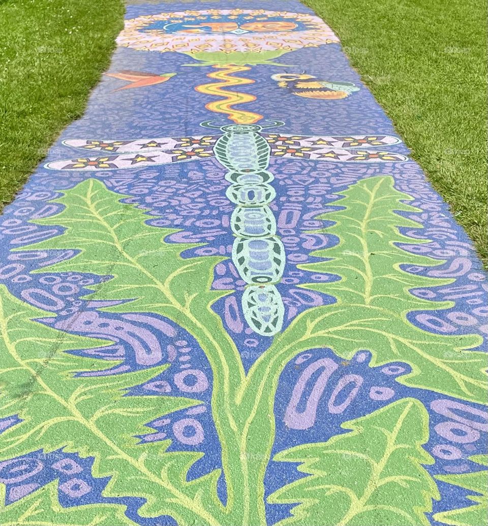 Pristine sidewalk art showcases a dragonfly, bumble bee, and bird gracefully hovering above lush green leaves, all set against a vivid purple background.