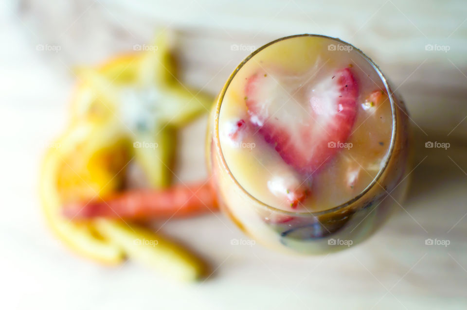 Dreamlike fresh  sweet vegetable smoothie with orange, carrots carambola, star fruit, honey yogurt swirls high angle view of heart shaped strawberry on top  yellow and orange Colors 