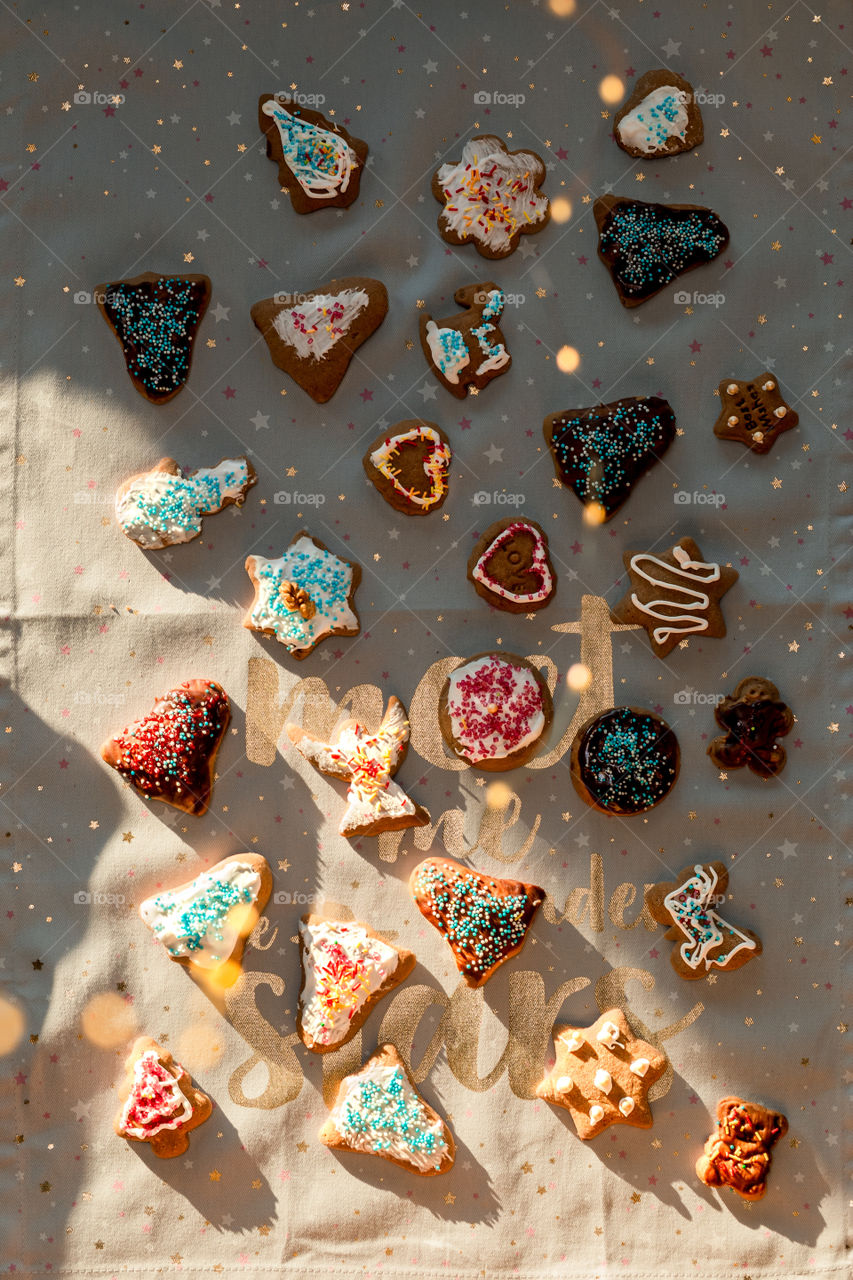 Christmas gingerbread cookies in many shapes decorated with colorful frosting, sprinkle, icing, chocolate coating, toppers, put on plain fabric
