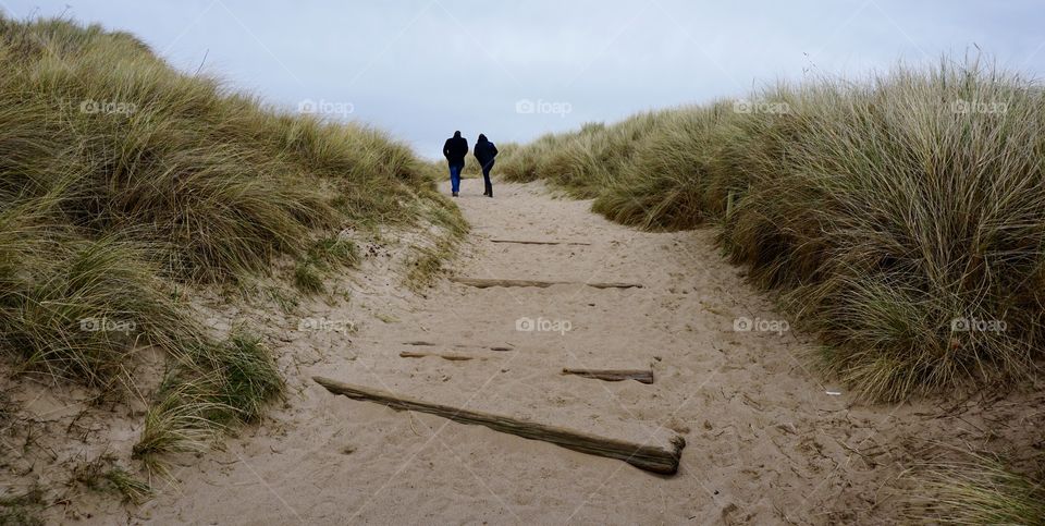 Couple walking to beach among grass sand dunes