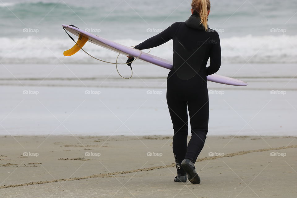 Let’s surf- young girl wearing diving suit and carrying a surfboard heading for an adventure 