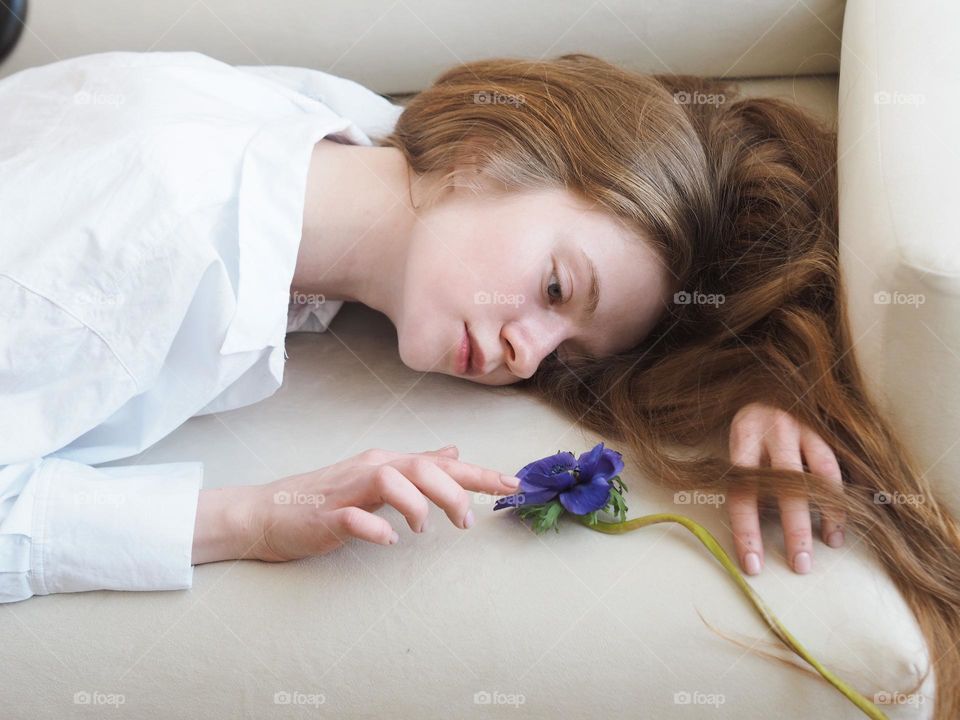 Young beautiful girl with flower lies on a white sofa at home