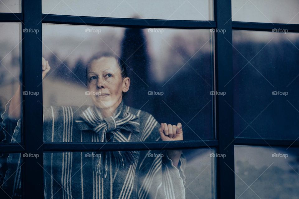 Portrait of mature woman looking through dirty window glass