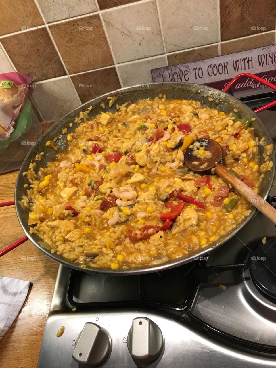 Paella cooking on the stove in kitchen with wooden spoon. 
