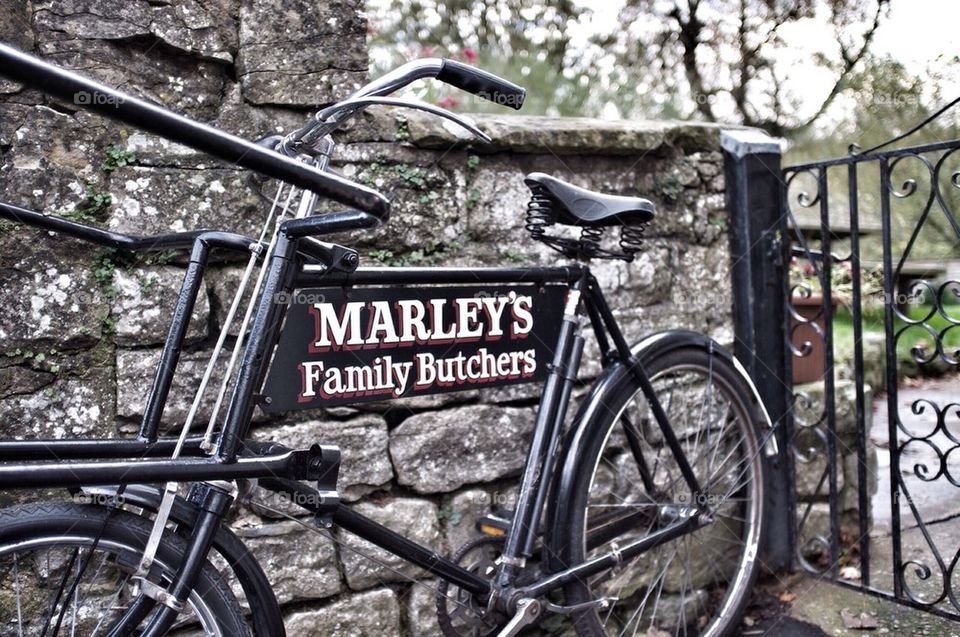 An old fashioned butcher's delivery bicycle leans against a stone