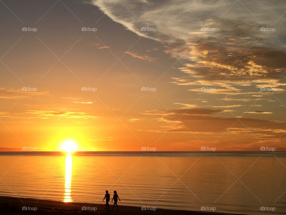 Couple walking silhouette at brilliant orange sunrise on beach at ocean 