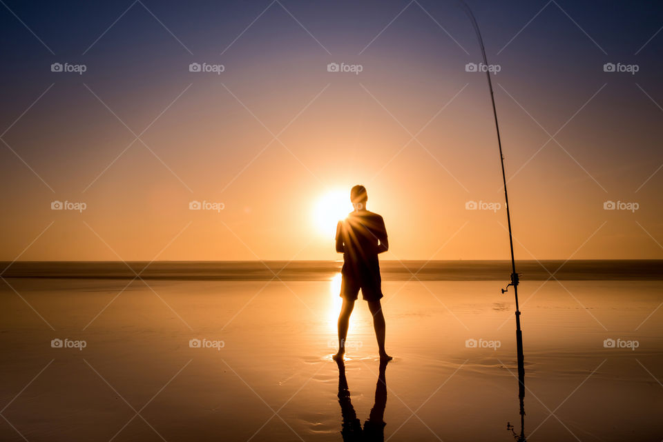 Silhouette of a person standing on beach with fishing rod