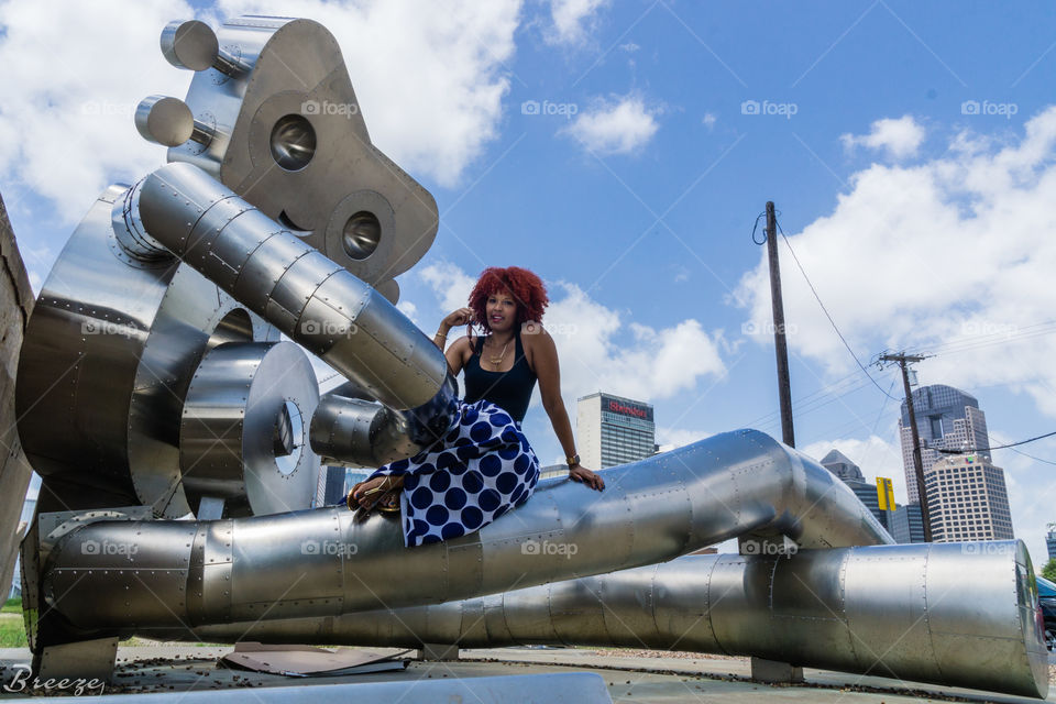 Woman sitting on travelling man statue in Dallas, Texas