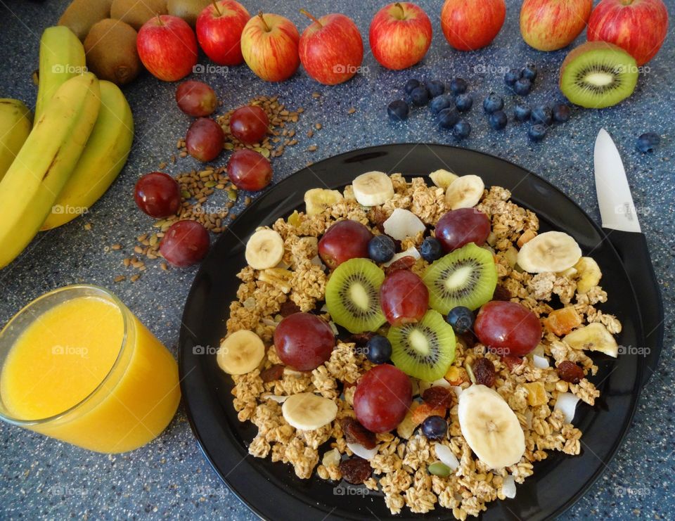 Healthy breakfast of crunchy flakes kiwi, banana, grapes, berries, raisins and fresh orange juicy drink