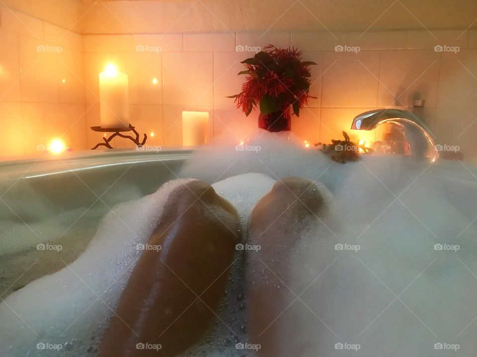 A selfie photo taken of a nude woman relaxing in a luxurious candlelit bubblebath .