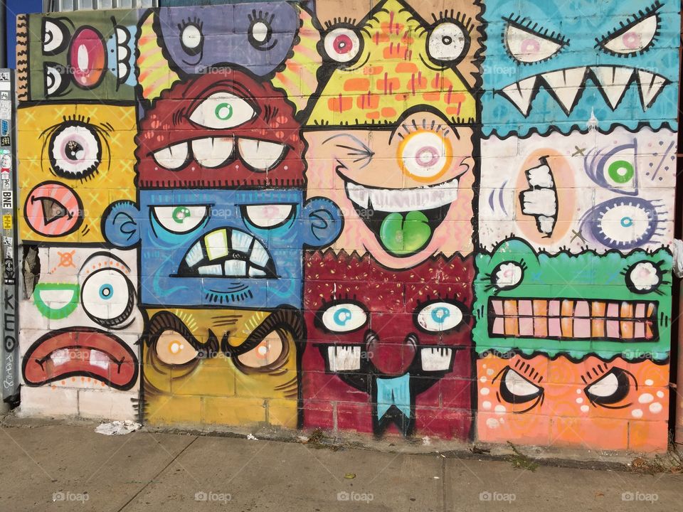 Picture of graffiti sprayed on brick wall in Brooklyn . Picture includes different faces of smilies and unique faces in detailed color. I don't know if it's vandalism but it's pure art.