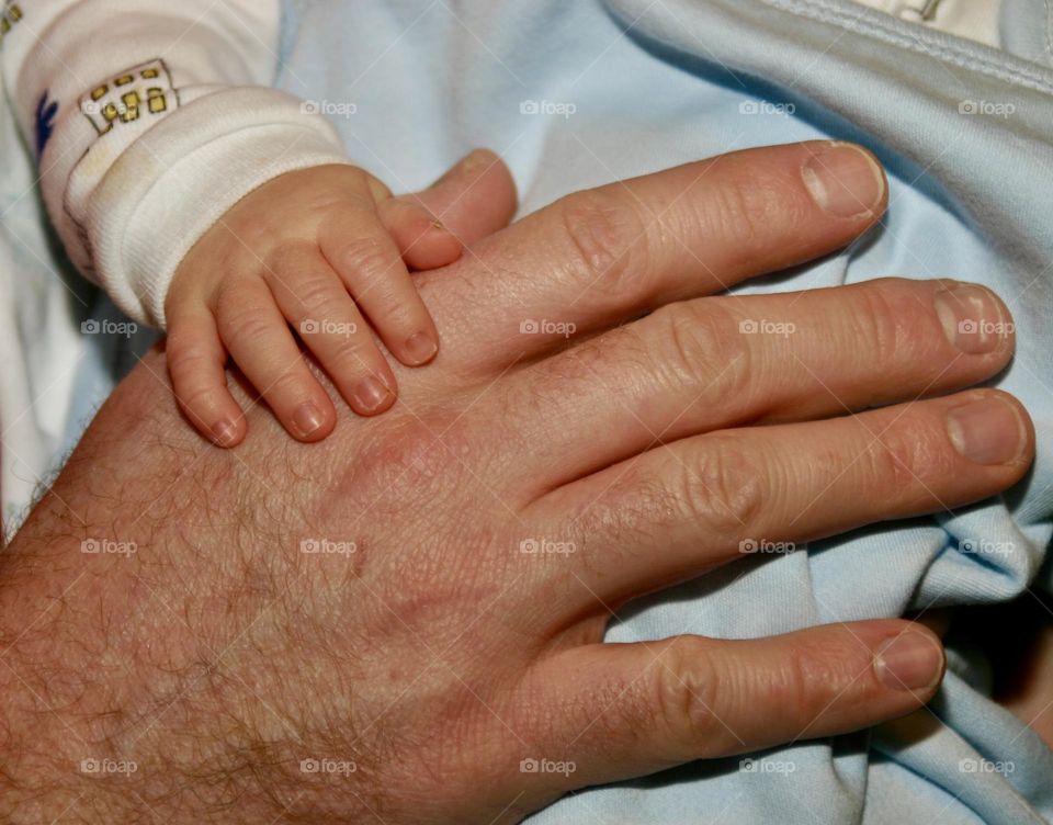 Father and infant son hand on hand 