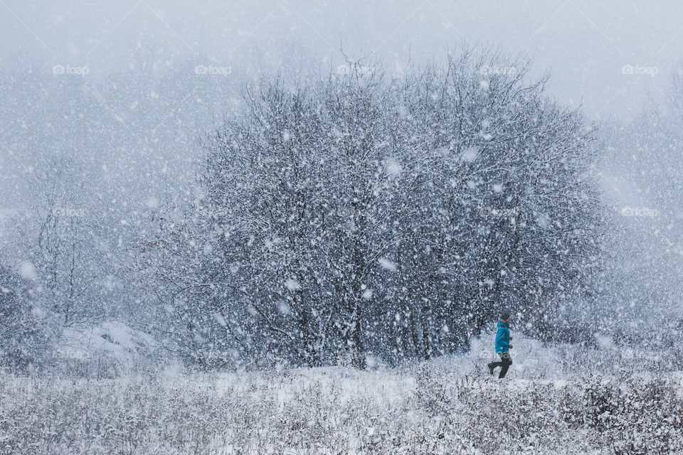 Young man jogging through meadow pathway during heavy snowing. Workout outdoors during winter snow storm