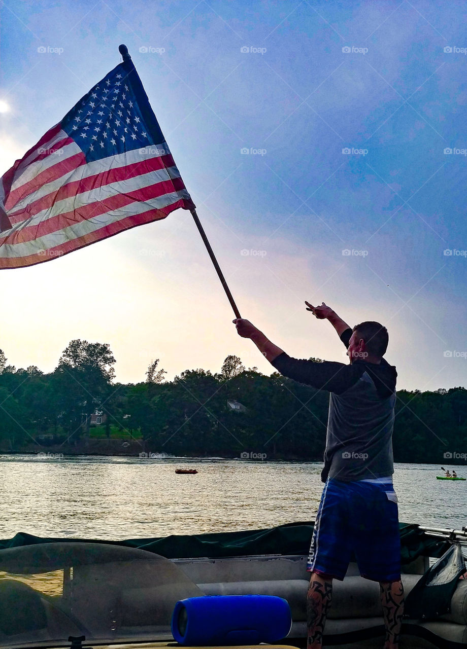 Man holds up American flag and salutes while on boat during sunset evening hour