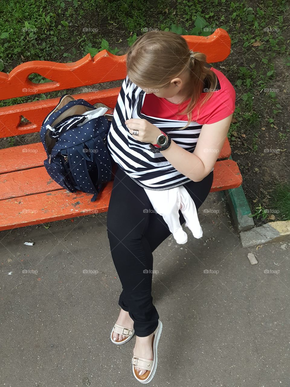 mother on the bench is feeding the baby with milk