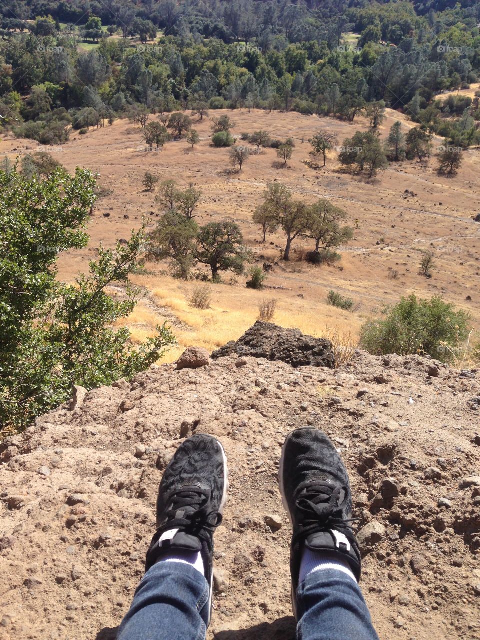 Close to the edge, dry, arid, cliff with a long view of the surrounding area. See trees, rolling hills, and a cliff. 