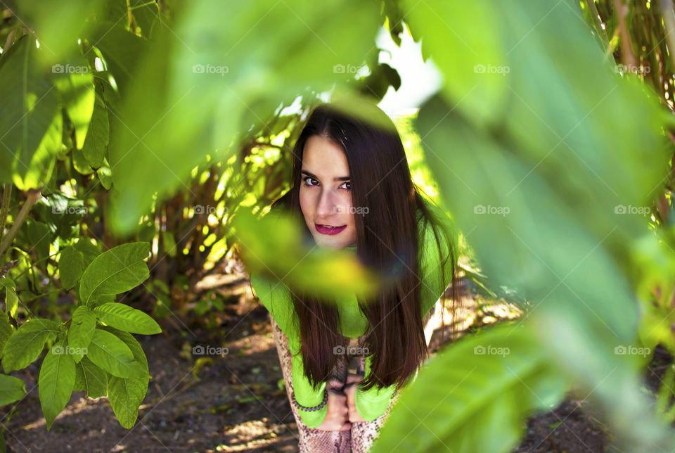 Cute attractive young woman looking at camera through leaves frame