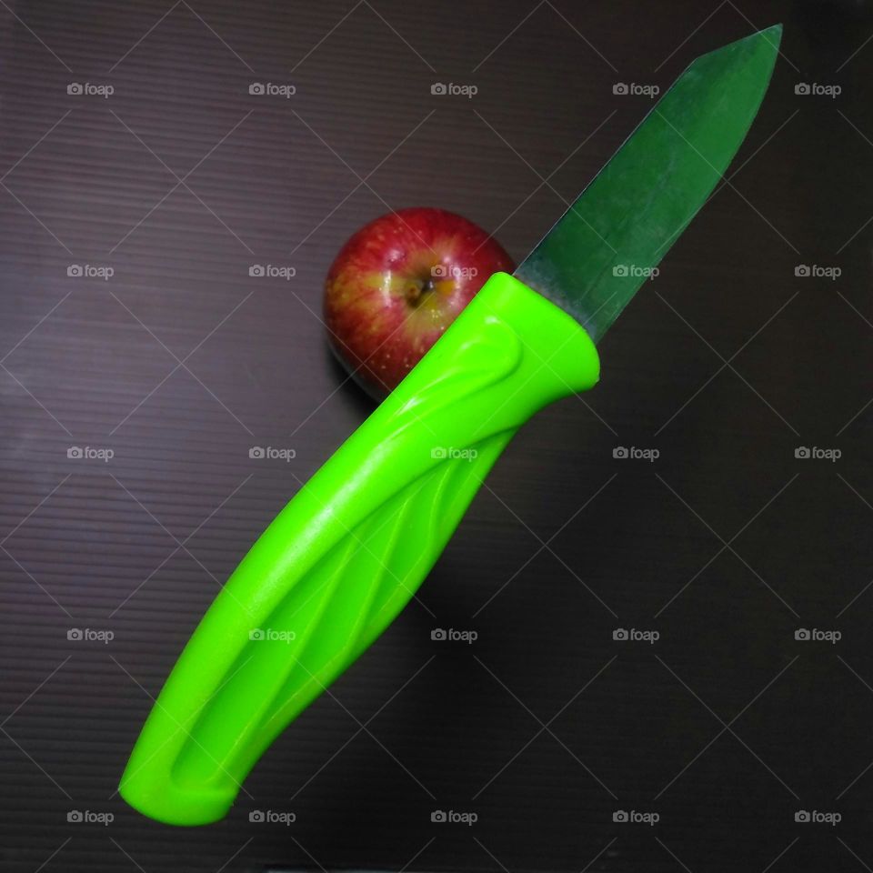 Green knife on red apple