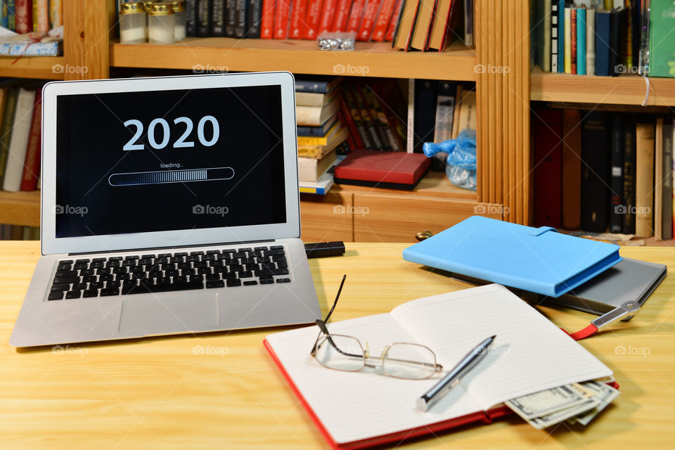 Text - 2020 loading and loading bar on laptop desktop, bookshelf, notebook, eyeglasses, pen,  new year concept