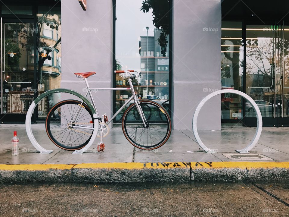 A fixie bicycle locked up on the street near a tow away zone in San Francisco.