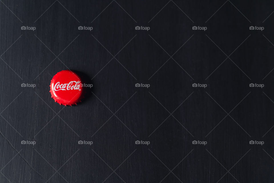 Coca-Cola bottle cap lies on a black wooden table.  strong, laconic, beautiful