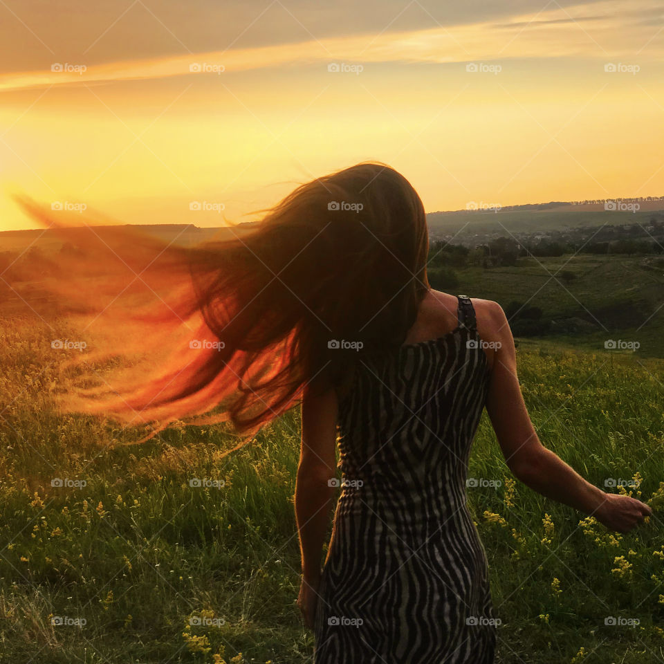 Red sunrise light in long hair if young woman in the field in the wind 