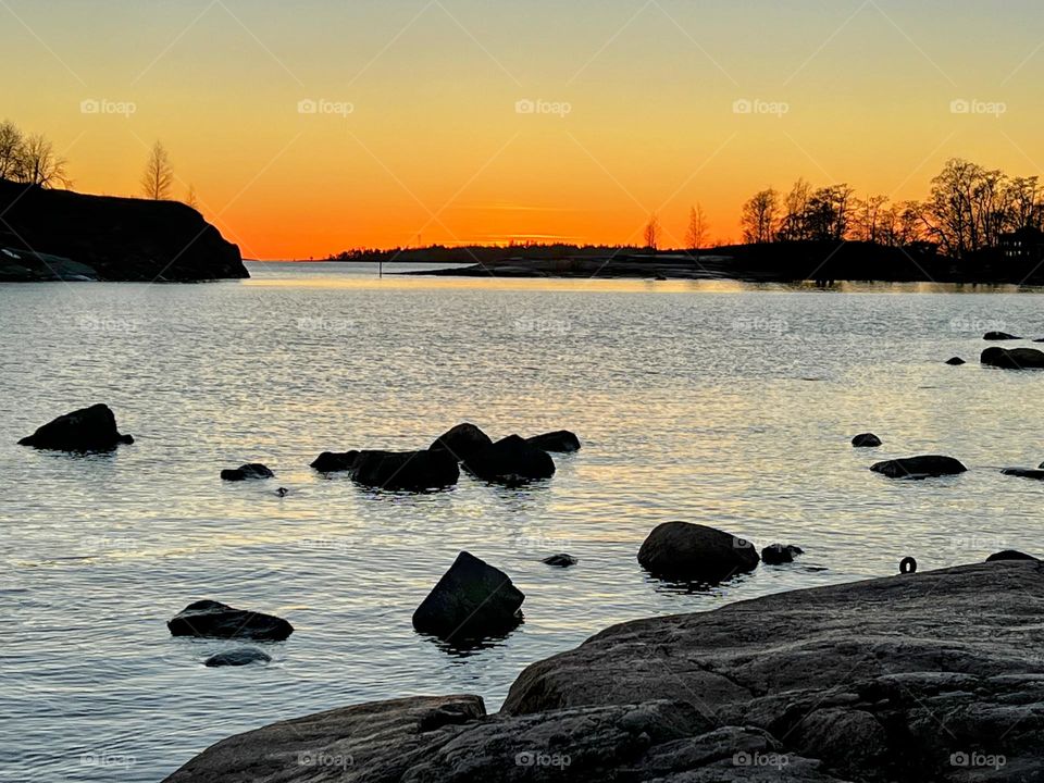 Tranquil silent landscape with rocky shore and stones silhouette and bright sunset horizon over the Baltic Sea on the background