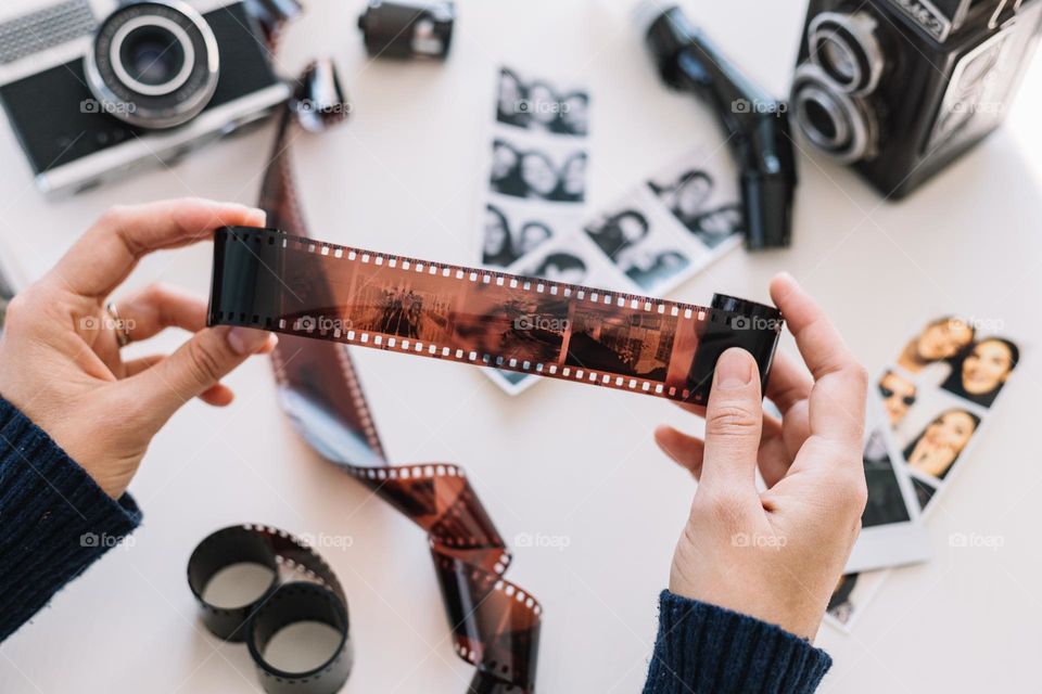 Hands of a woman holding a developed film roll, while surrounded by film cameras and other rolls, in her photo studio. 