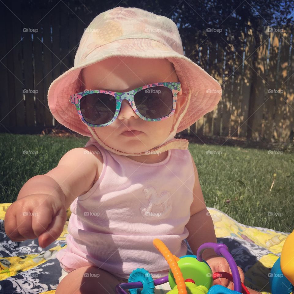 Baby kid in hat and sunglasses sitting with toy