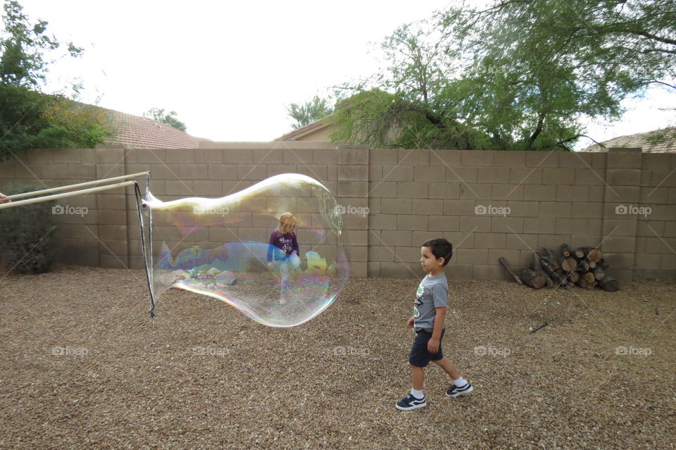 Girl looks like she is in the giant bubble that the little boy is staring through.