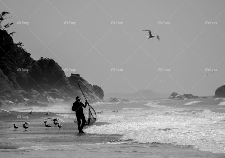 Silhouette of a man fishing with his net with mountains and birds in the background.
