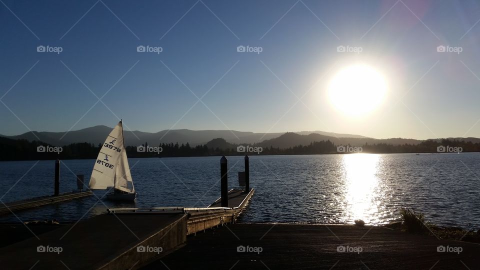 low sun over lake with dock and sail boat