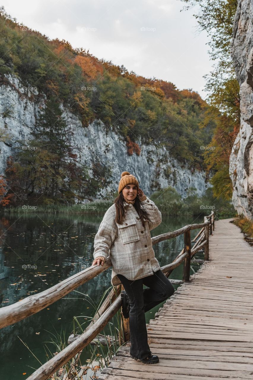 Portrait of happy girl standing on wooden footpath by lake in autumn