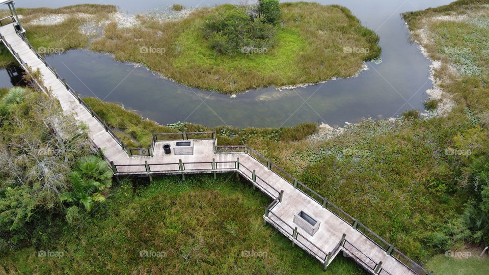 A dock going over grass and a meandering water source over a swampy environment 