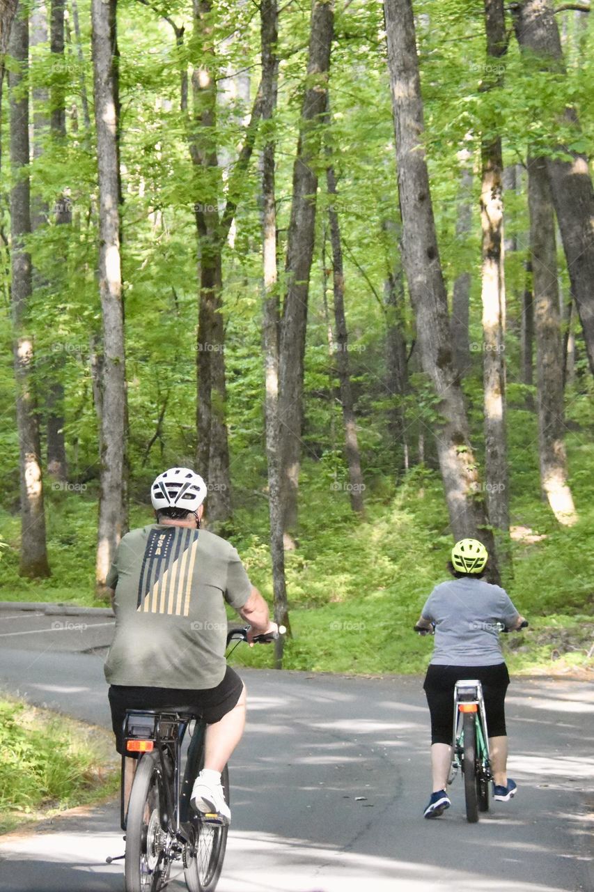 A man and woman riding their bikes on a forest road