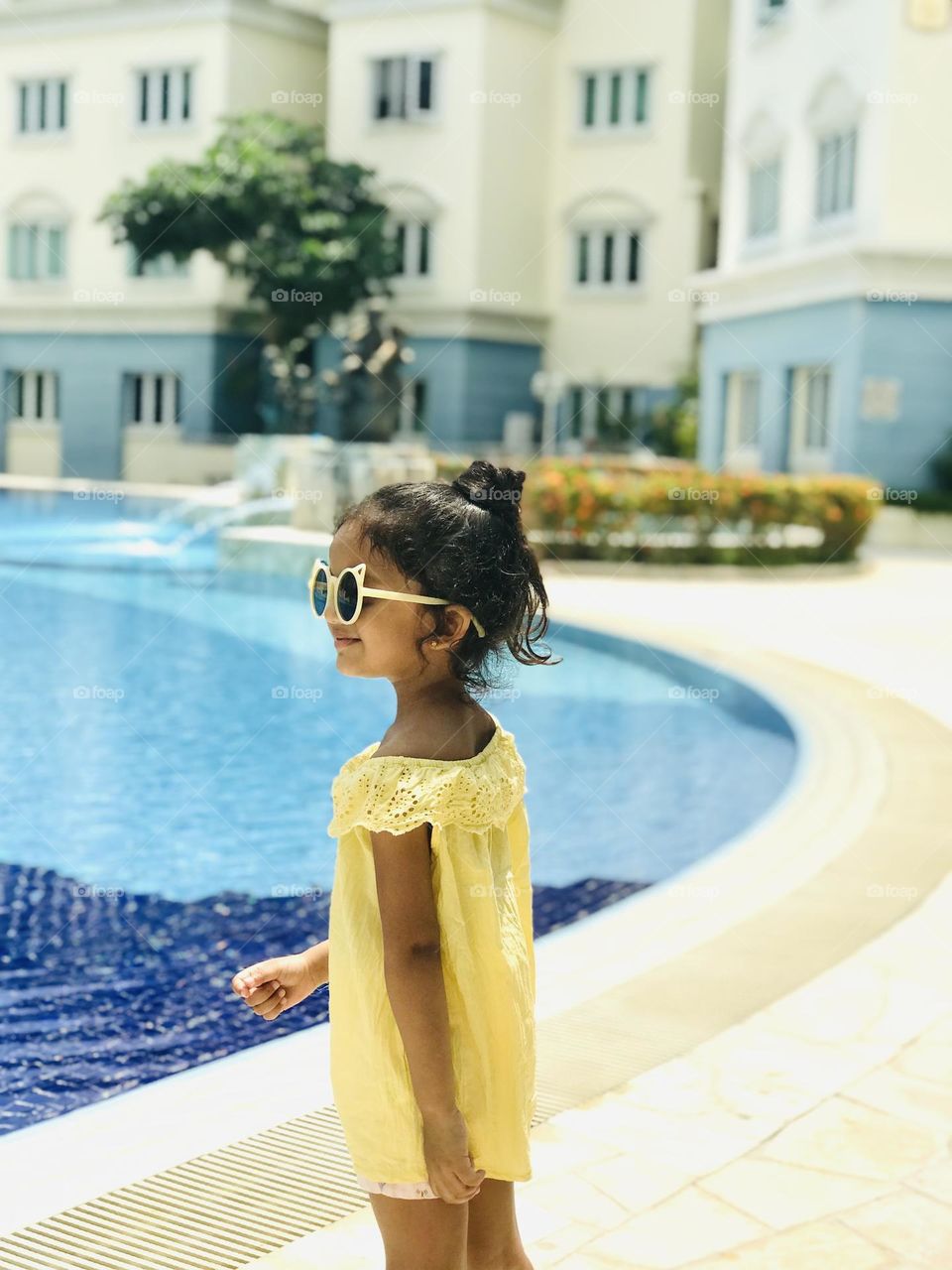 A cute girl standing near swimming pool in a summer outfits and wear sunglasses.