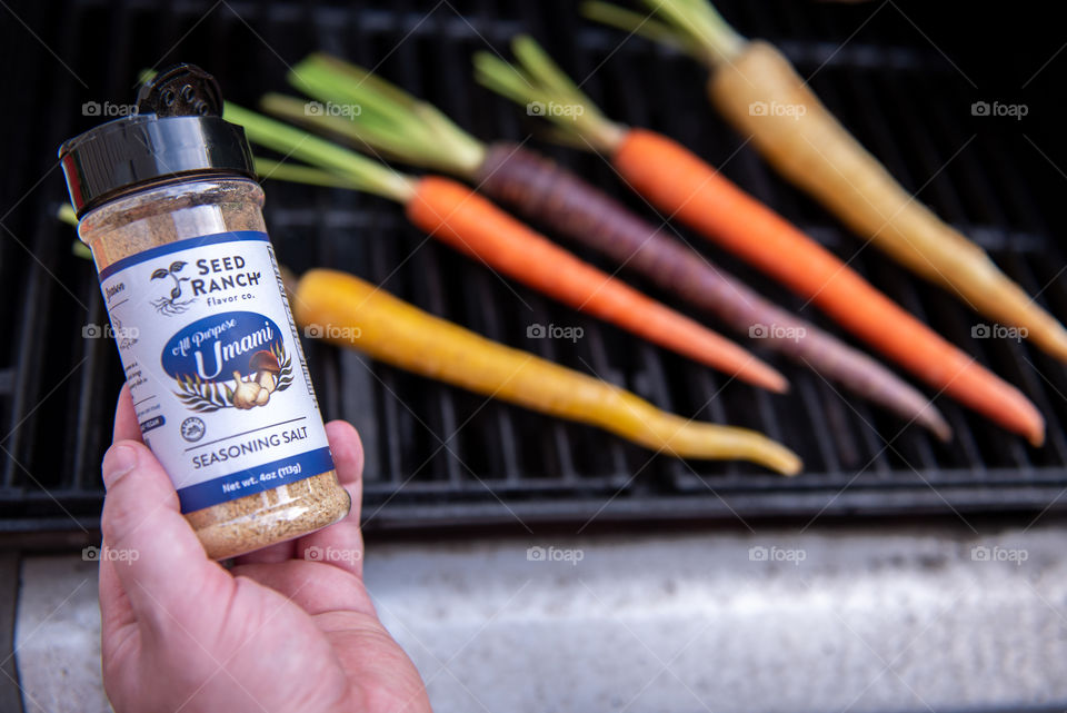 Person holding a bottle of Seed Ranch umami seasoning while grilling carrots 