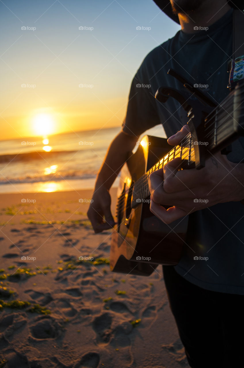 A man plays guitar on a beach during sunrise