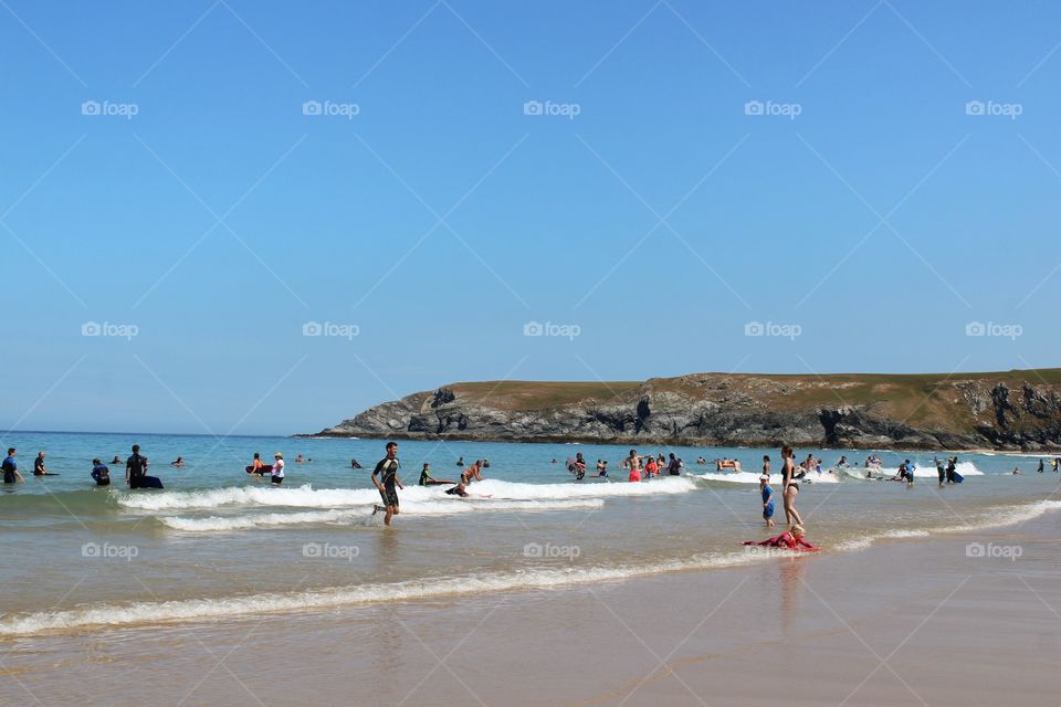 People playing in the sea on a busy beach in Cornwall on a sunny summers day