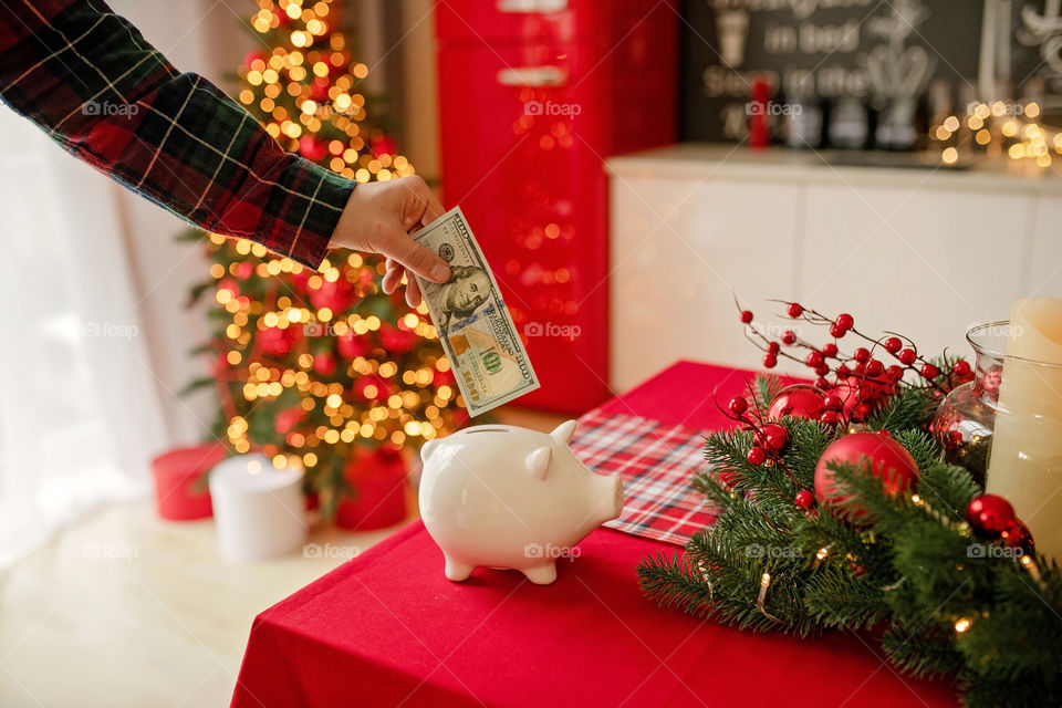 piggy bank with 100 dollars banknote in festive New Year atmosphere of scenery.  Magical bokeh with Christmas tree and bright lights.