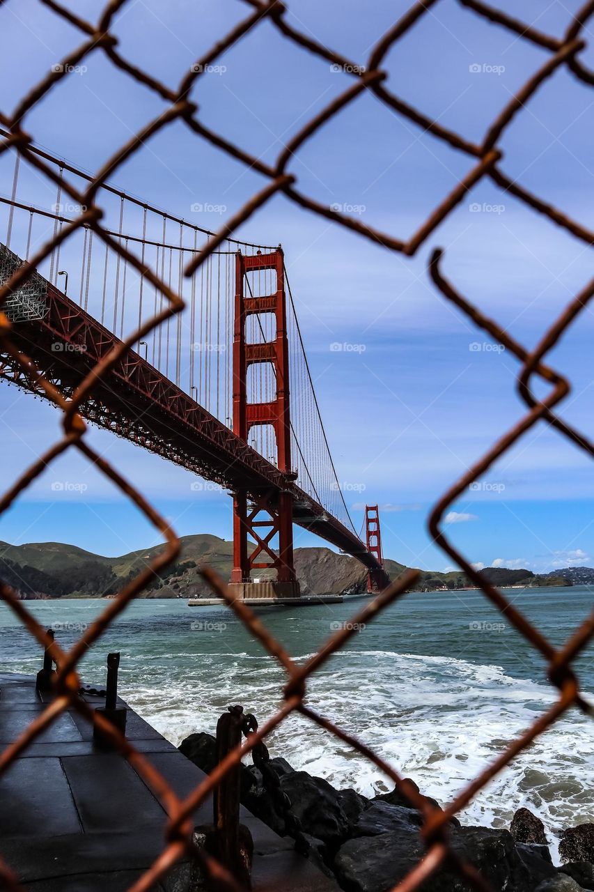 Golden Gate Bridge in San Francisco California seen through a rusty metal wire fence on a clear day still looking majestic at the Fort Point viewing area 