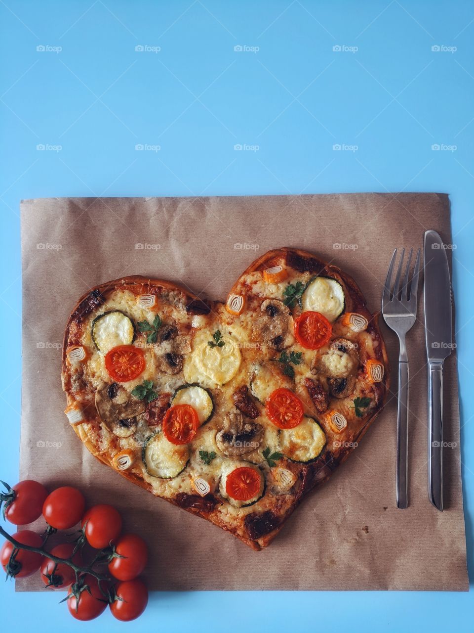 Delicious vegetarian pizza in the shape of a heart for Valentine's Day with tomatoes, vegetables and cheese on a blue background.