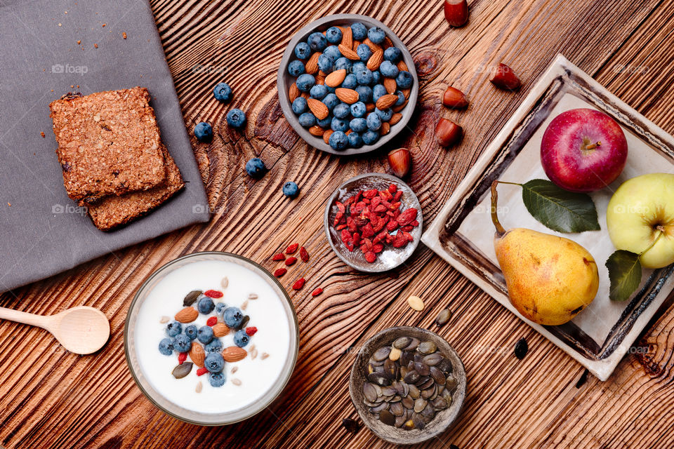 Breakfast on table. Yogurt with added blueberries and roasted almonds. Muesli cookie, apples and pears on wooden table. Light and healthy meal. Good quality balanced diet. Flat top-down composition