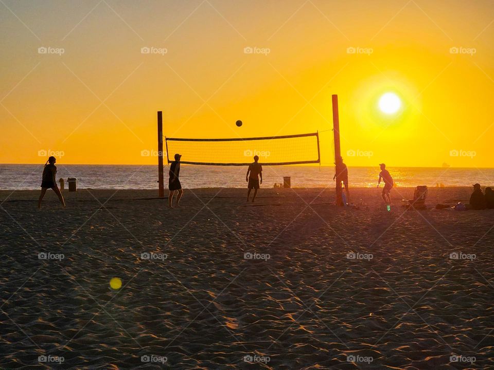 The afternoon summer sun casts light on people playing beach volleyball on a Southern California beach