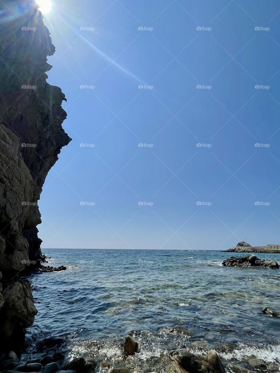 Sun peaking out behind the cliffs on a sunny Greek Island