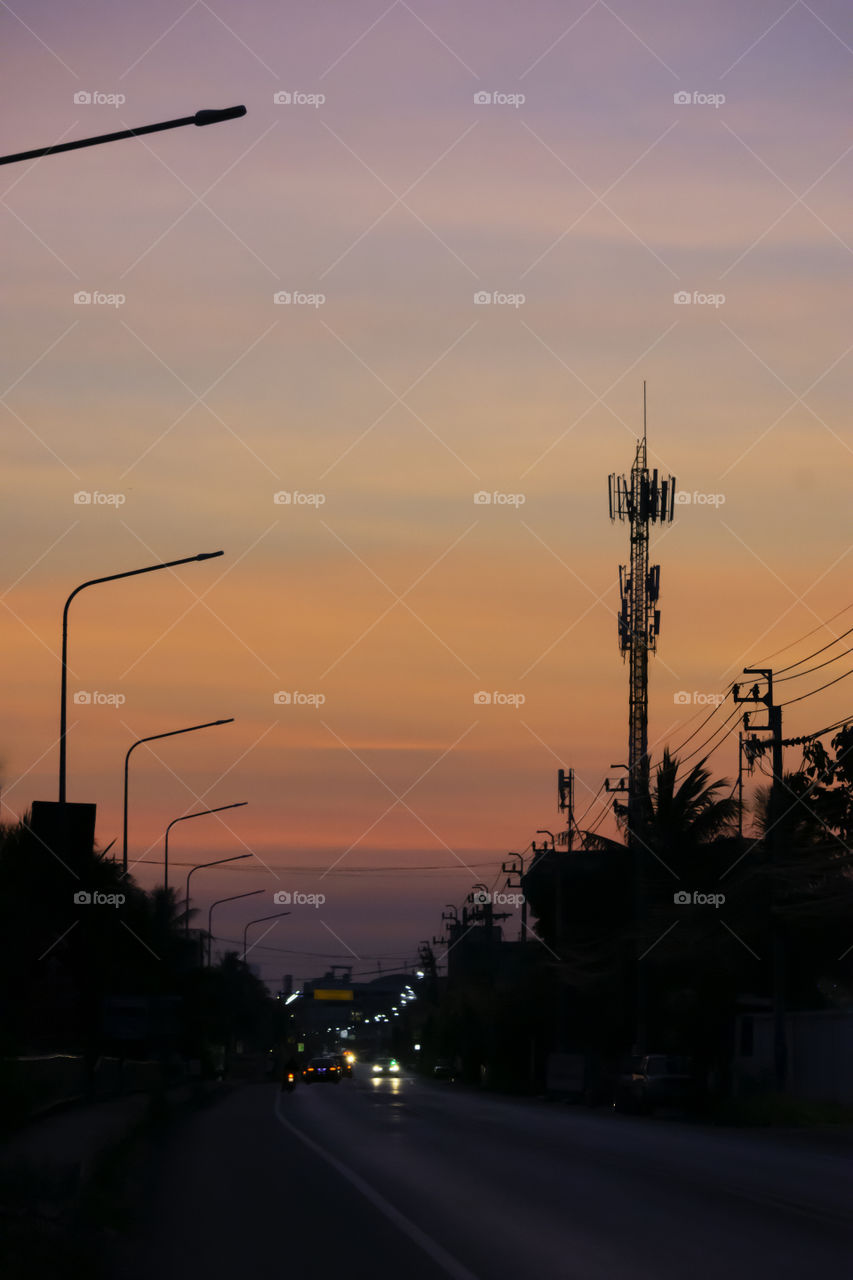 The sunrise in the morning is orange after the telephone receiver antenna and the road.