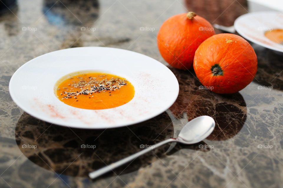 pumpkin soup in a round plate and round pumpkins nearby, a gray table and white dishes