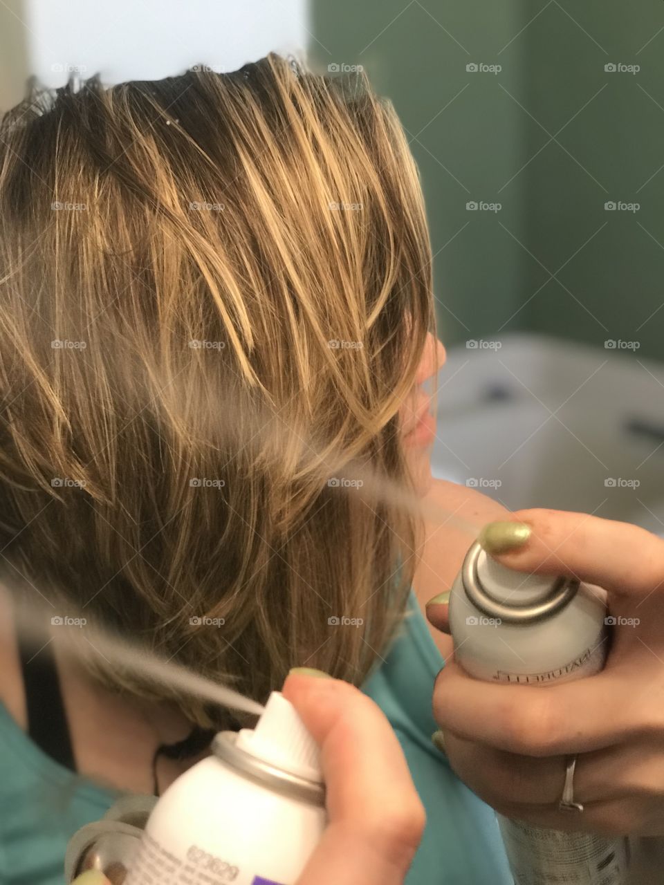 Woman fixing hair with spray in a bathroom getting ready for the day. 