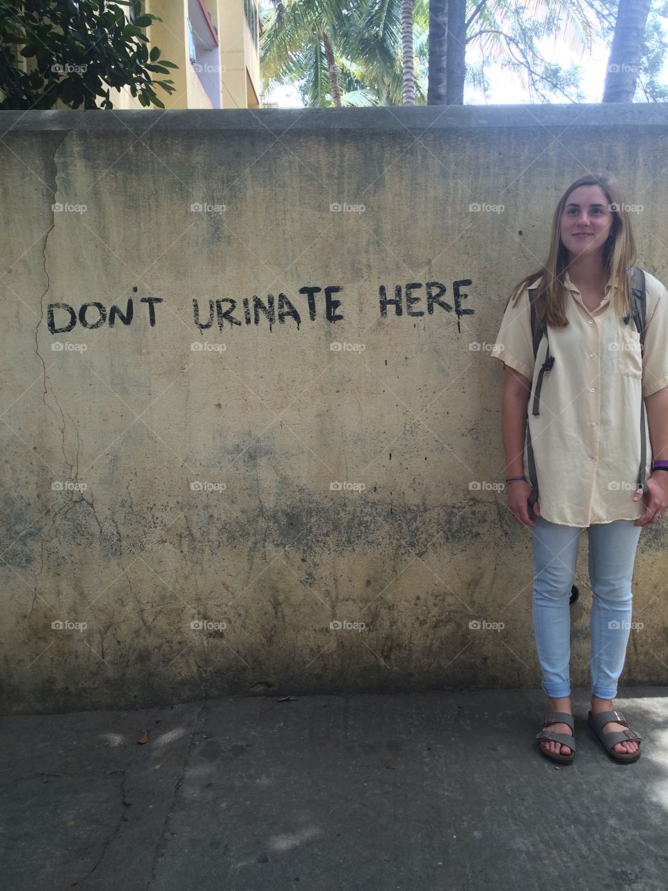 "Don't urinate here" hand painted on a wall in southern India. A young traveler standing mischievously beside it. 