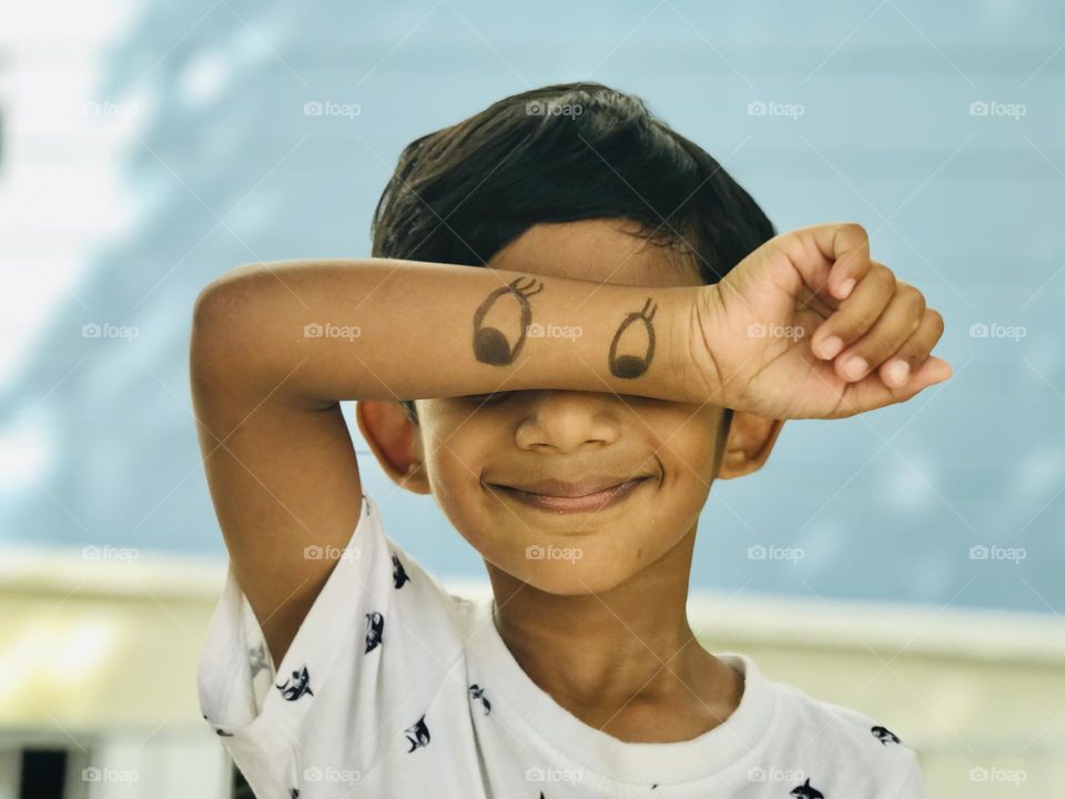 Fun with kids,a boy cover his eyes by drawing a cartoon eyes on his hand.